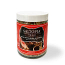 A clear jar with a white lid labeled SALTOPIA Infused Sea Salts Steak Bundle - Searingly Great Flavors on a red background, featuring steak and seasonings, brings steakhouse-style taste to your favorite dishes.
