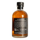 A clear glass bottle filled with amber chili oil, labeled Spice Witch Chili Oil by Spice Witch. The black label highlights its savory flavor and versatility, made with avocado oil, and includes a QR code and website link.