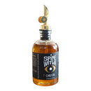 A glass bottle of Spice Witch Chili Oil by Spice Witch with a gold spout dispenser. The label shows a stylized eye and spotlights its savory, avocado oil-based flavor. You can see the amber-colored chili oil inside the bottle.