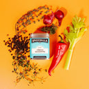 Spicewalla Creole Seasoning tin by Spicewalla is pictured with fresh thyme, black peppercorns, red onions, red chili pepper, and celery on an orange background—ideal for authentic Louisiana dishes or adding bold flavor to gumbo.