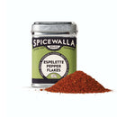 A metal tin of Spicewalla Espelette Pepper Flakes by Spicewalla sits beside a vibrant pile of smoky red pepper flakes, displayed on a white background.