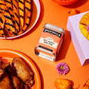 Spicewalla hot honey BBQ rub can on an orange table with grilled items and a pink flower.