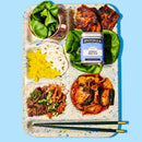 A colorful tray with spinach in a cup, grilled chicken, Spicewalla Korean BBQ Rub by Spicewalla, sliced lotus root, yellow pickled radish, rice with beef and scallions, kimchi, and a pair of chopsticks.