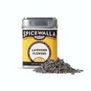 A Spicewalla Lavender Flowers metal tin from Spicewalla rests on a white surface, with dried lavender buds for baking or culinary lavender recipes scattered in front of the container.