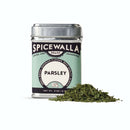 A Spicewalla Parsley metal tin sits beside a small pile of dried flat leaf parsley flakes, highlighting the brand's vibrant color and fresh herb flavor against a white background.