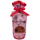 A pink gift bag with a red ribbon and black snowflakes holds Terrapin Ridge Farms' Holiday Grab and Go Giftset, featuring Onion Blossom Horseradish Dip and Braided Pretzel Twists. A small round window reveals the treats inside.