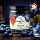 A jar of Texan Heartland Blueberry Royale Jam sits on a table surrounded by fresh blueberries. The label highlights this gourmet jam’s use of Grand Marnier liqueur, with the Scovie Awards logo in the upper right corner.