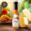 A bottle of Texan Heartland Caribbean Pineapple Hot Sauce sits on a table beside pineapple slices, with tortilla chips and peppers in the background. The Hot Sauce Fest ATL badge appears in the top left corner.