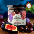 A jar of Texan Heartland Cherry Fig & Port Wine Jam sits among fresh cherries and figs, with sliced fruit in the foreground—ideal for pairing with artisan cheese. The decorative label displays the Texan Heartland brand and an award badge.