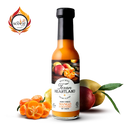 A bottle of Texan Heartland Honey Ginger Mango Habanero Hot Sauce is shown with fresh mangoes and habaneros; its vibrant orange color and spicy-sweet condiments award logo enhance its tropical, flavorful appeal.