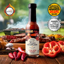 A bottle of Texan Heartland Lone Star Reserve Hot Sauce sits on a table with red chili peppers, sliced bell pepper, and grilled food. 2025 hot sauce competition award badges surround the Texan Heartland bottle.