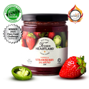 A jar of Texan Heartland Vanilla Strawberry Jalapeno Jam is displayed with a label showing strawberries and jalapeños. Fresh strawberries, a sliced jalapeño, and award badges are arranged beside this spicy jam by Texan Heartland.