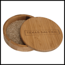 The Texas Salt Co. Cocktail Wood Cellar is a round bamboo salt container with a sliding lid, partly open to display coarse salt inside. The lid features the engraved words TEXAS SALT CO.