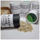 Several Texas Salt Co. Jalapeño Lime Cocktail Salt containers are arranged, one spilling spicy citrus rim salt onto a white surface. A wooden bowl filled with margarita rim salt is partially visible nearby.