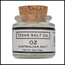 A small glass jar with a cork lid labeled Texas Salt Co. Oz Australian Salt, Net Wt .5oz (14g), perfect natural sea salt for cooking, is shown on a white background.