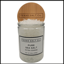 A 15 oz (425g) clear glass jar of Texas Salt Co. Pure Extra Coarse Sea Salt, labeled with the brand and topped with a bamboo lid—ideal for grinders or use as dry brining salt, filled with large white sea salt crystals.