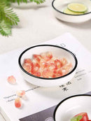A Texas Salt Co. Round Dipping Dish filled with pomegranate seeds rests on an open book, scattered seeds nearby. Another dish with lime slices and green leaves from Texas Salt Co. is partially visible in the background.