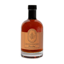 A glass bottle of Under The Bark Syrup Co Bourbon Maple Syrup features 100% pure maple syrup infused with bourbon, amber in color, with a tan label and maple leaf logo, black cap, and made in Minnesota.