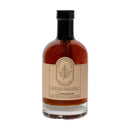 A clear glass bottle of Under The Bark Syrup Co Cinnamon Maple Syrup, labeled 100% Pure Maple Syrup, Cinnamon. The label features a leaf logo and highlights this Minnesota-made flavored syrup, 12.5 fl oz.