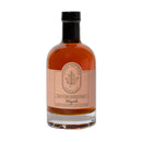 A clear glass bottle with a black cap, filled with Under The Bark Syrup Co Pure Maple Syrup. The label features a maple leaf illustration, reads "100% Pure Maple Syrup," and notes it is authentically made in Minnesota.