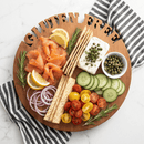 The Words With Boards Gluten Free Round Cutting Board (14" diameter) by Words with Boards, LLC is shown labeled "GLUTEN FREE" and topped with smoked salmon, lemon, red onion, crackers, tomatoes, cucumber, capers, cream cheese & rosemary. A striped napkin sits nearby.