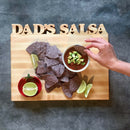 The Words With Boards Personalized Cutting Board Small 9.5" x 12.5" by Words with Boards, LLC features cutout text and is shown serving chips, lime wedges, and salsa—making it a unique kitchen gift.