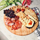 The Words With Boards Seriously Gluten Free Round Personalized Cutting Board (14" by Words with Boards, LLC) displays grapes, crackers, cured meats, cheese, dip, and wooden “LEISLER” and “Seriously GLUTEN FREE” letters—perfect for gluten free gatherings.