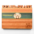 The Words With Boards Wedding Bells Personalized Cutting Board (12.5" x 16") by Words with Boards, LLC features your names cut out at the top, engraved wedding bells in the corner, and a green "WORDS WITH BOARDS" label across the middle—ideal for weddings.