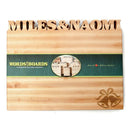 The Words With Boards Wedding Bells Personalized Cutting Board (12.5" x 16") by Words with Boards, LLC features MILES & NAOMI carved at the top and wedding bells in the corner—an ideal wedding gift. A green band with "WORDS with BOARDS" decorates the center.