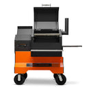 The Yoder Smokers YS480S Competition Pellet Grill features black and orange styling, stainless steel shelves, a digital control panel, front handle, wheels, and an open lid showing the cooking rack—ideal for competition pellet grill enthusiasts.