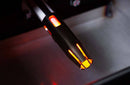 A close-up of a metallic espresso machine part, glowing orange with heat, mirrors the intense radiance of a Yoder Smokers YS480S Competition Pellet Grill with Stainless Steel Shelves. Illuminated slits reveal bright internal heating elements above metal.