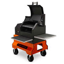 The Yoder Smokers YS480S Competition Pellet Grill features stainless steel shelves, a black and orange design, wheels for easy mobility, and an open lid for food prep—ideal for serious outdoor grilling performance.