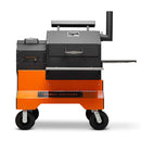 The Yoder Smokers YS480S Competition Pellet Grill with stainless steel shelves offers direct-flame grilling and smoking versatility, featuring a black and orange design, chimney, side handle, and signature branding.
