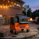 A Yoder Smokers YS640S Competition Pellet Grill with Wire Shelves stands on a stone patio at dusk, under string lights, with a fire pit and seating nearby—perfect for cozy, wood-fired BBQ gatherings.