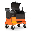 The Yoder Smokers YS640S Competition Pellet Grill by Yoder Smokers features wire shelves, a hinged lid, side firebox, chimney, metal cooking grates, and large wheels for mobility. Shown on a white background.