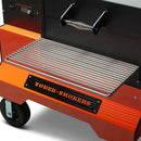 Close-up of the Yoder Smokers YS640S Competition Pellet Grill with Wire Shelves, featuring a clean metal grate, sturdy handle, black and orange logo, and wheels for easy portability. Renowned for delivering rich wood-fired flavor.