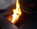 Bright flames rise from an open rectangular compartment inside a metal structure, possibly a Yoder Smokers YS640 with the Yoder Smokers YS640 Two-Piece Heat Diffuser, set against a dark background.