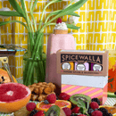Spicewalla spice set with a colorful background featuring fruits and a plant.