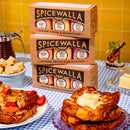Three Spicewalla 3 Pack Signature Sugar Collection boxes stacked on a table with French toast, strawberries, butter, baking sugars, sugar cubes, syrup, and a frog figurine playing guitar. The background features yellow tiles.