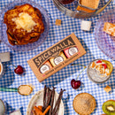 A picnic table featuring pancakes, fruit, chia pudding, cherries, vanilla beans, cinnamon sticks, spice jars in a Spicewalla box, and the Spicewalla 3 Pack Signature Sugar Collection by Spicewalla on a blue checkered tablecloth.