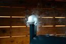 A silver Baseball Batting Helmet BBQ Chimney Cap by Pimp My Grill sits atop a grill stack with smoke rising.