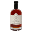 A glass bottle of Under The Bark Syrup Co Smoke Maple Syrup with a black cap, amber syrup, and a label featuring a leaf design—ideal as a distinctive cocktail syrup.