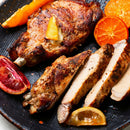 Grilled pork chops—one whole, one sliced—are served on a dark plate with orange, lemon, and blood orange slices, featuring a golden-brown crust seasoned with SALTOPIA Infused Sea Salts’ Saltopia Smoked Alderwood, Grapefruit & Garlic Salt.