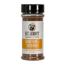 A clear plastic bottle of B.T. Leigh’s Gluten-Free Taco Seasoning containing brown vegan seasoning, featuring a label with a cartoon of a man in a baseball cap and the text Somethin to Taco Bout artisan taco seasoning.