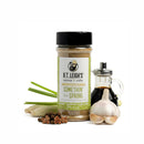 A bottle of B.T. Leigh’s Asian Inspired Lemon Pepper Seasoning surrounded by lemongrass stalks, whole peppercorns, star anise, a bulb of garlic, and a small glass carafe of soy sauce.