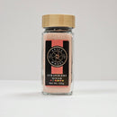 A clear glass jar with a bamboo lid containing pink Spice Wheel Strawberry Sugar, made from granulated sugar and strawberry powder. The black label displays the Spice Wheel branding, product name, and a net weight of 105g.