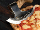 A thin-crust pizza topped with melted cheese and tomato sauce is sliced using the Texan Knives Custom Hand Engraved Ax Pizza Cutter, featuring Norse runes on its 8-inch J2 steel blade—a unique kitchen tool for food lovers.