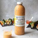 A bottle of Terrapin Ridge Farms Zesty Seven Spice Dressing sits on a table beside a small glass of dressing and sushi hand rolls filled with vegetables and protein, showcasing this flavorful, Asian-inspired dressing.