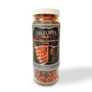 A jar of SALTOPIA Infused Sea Salts labeled BBQ Blend: HE MAN, featuring coarse reddish-brown salt crystals for the perfect smoky hickory sea salt finish on grilled meats and herbs.