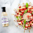A platter of vibrant appetizer skewers is arranged around a bowl of creamy salad dressing, with a bottle of Terrapin Ridge Farms Sweet Red Onion White Balsamic Dressing displayed nearby.